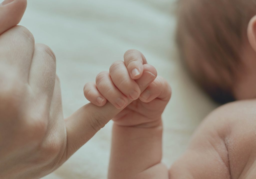 Mãe atenciosa segura com o dedo a mão de seu bebê em gesto de atenção e carinho